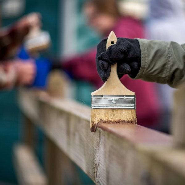Student applies paint to a wooden fence at Muskegon State Park
