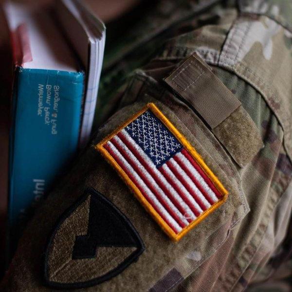 穿着印有美国国旗的军装的人的手臂上拿着书.